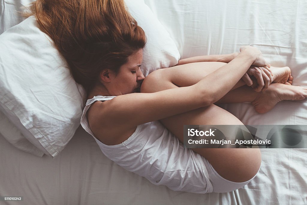 Lying down and sad Young woman lying down in fetus position Menstruation Stock Photo