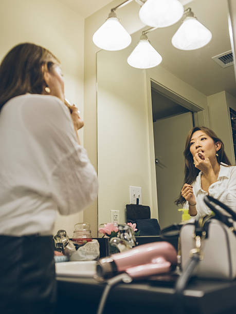 Young woman applying lipstick, looking in mirror