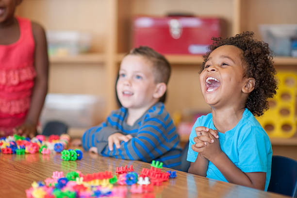 Laughing Together in Class A multi-ethnic group of elementary age children are playing with toy blocks together at a table. children laughing stock pictures, royalty-free photos & images