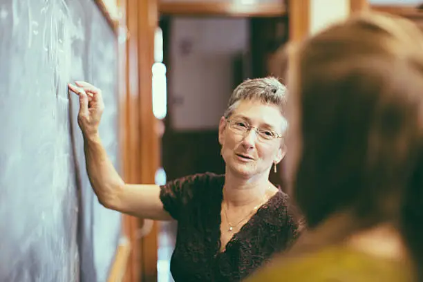 Photo of School teacher at chalkboard explaining math teenage student