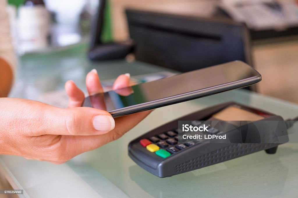 Woman paying with NFC technology on mobile phone at beautician Female's hand using contactless smartphone to pay in a store Mobile Payment Stock Photo