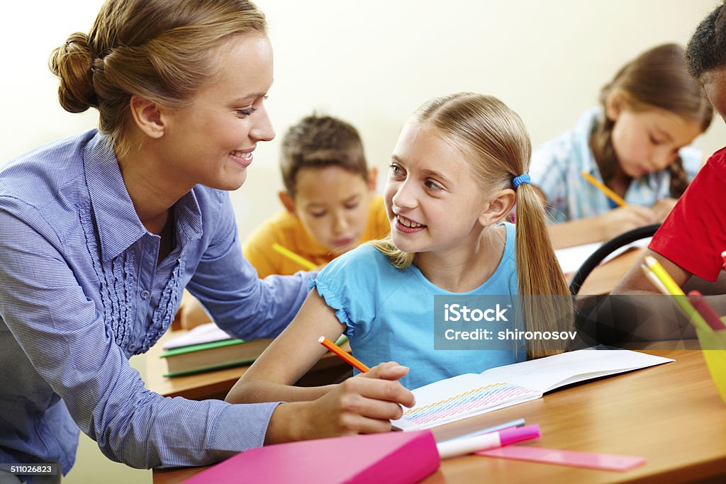 Pupil and teacher Portrait of smart girl and her teacher looking at each other at lesson in classroom Adult Stock Photo