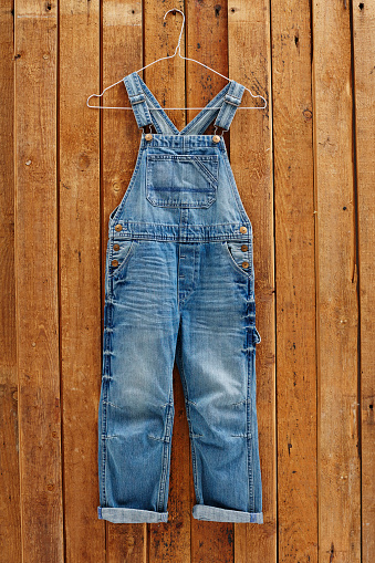 Pair of denim dungarees hanging against wooden wall