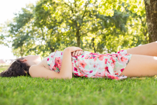 Stylish peaceful brunette lying on a lawn in a park on a sunny day