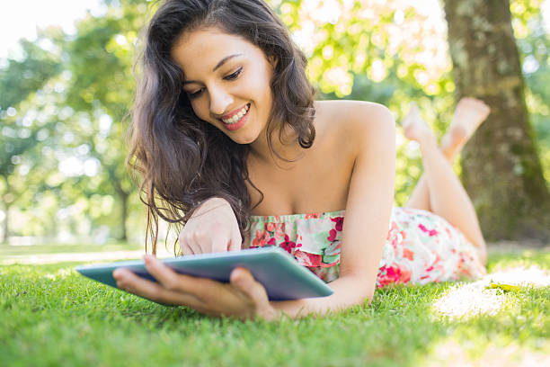 istock Stylish cheerful brunette lying on a lawn using tablet 511029185