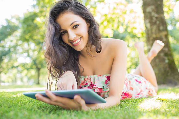 istock Stylish smiling brunette lying on a lawn using tablet 511029187