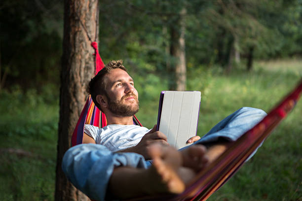 allegro uomo in amaca con digital tablet - men reading outdoors book foto e immagini stock