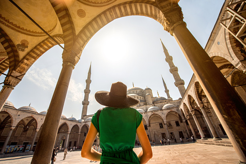 Young woman traveler in black hat and green dress looking on amazing Blue Mosque in Istanbul, Turkey