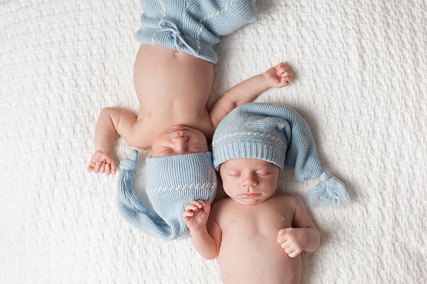 Sleeping Twin Baby Boys One month old fraternal, twin baby boys wearing light blue stocking caps and sleeping on a white blanket. twin stock pictures, royalty-free photos & images
