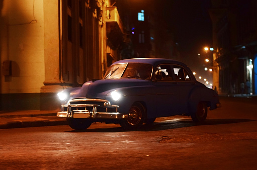 Front/left side shot on the old classic American car driving on the Havana street at night.
