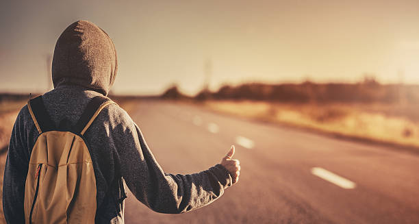 Hitchhiking traveler trying to stop the car on road Hitchhiking traveler with backpack trying to stop the car on road standing in the field. Stock photo. hitchhiking stock pictures, royalty-free photos & images