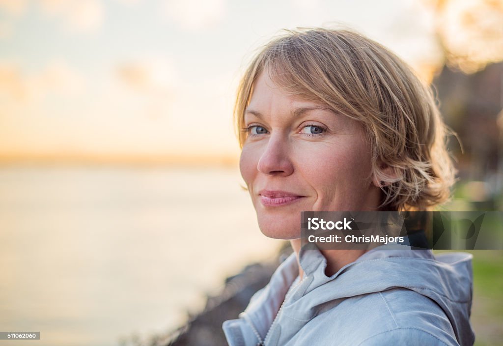 Mid 30's Woman with strong smile at sunset. Blonde, short hair, blue eyed, mid 30's woman gives a strong contented smile as the sun sets behind her. Women Stock Photo