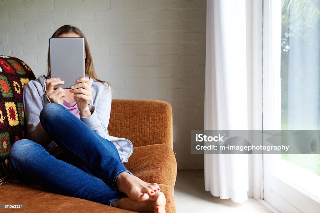 Woman holding tablet in front of face at home Portrait of a woman holding tablet in front of face at home Reading Stock Photo