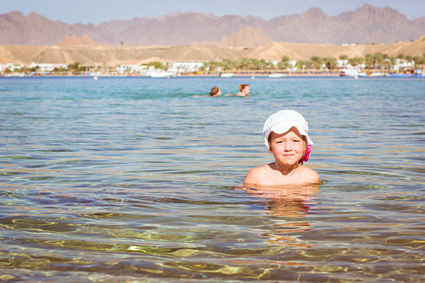 istock Girl in white hat sitting in water in middle beach 511068996