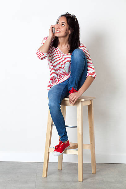 istock young multi-ethnic girl smiling on mobile, sitting on stool 511071294