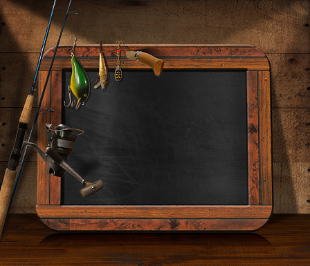 Empty blackboard with fishing tackle and folding knife on a wooden table and wooden wall