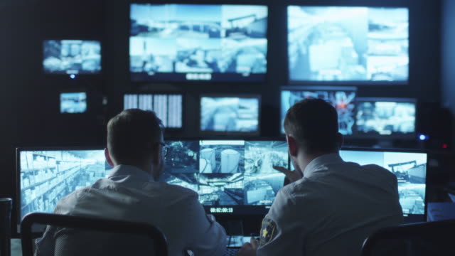 Two security officers noticed a trespasser on a surveillance computer screen in a dark monitoring room.