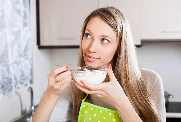 Smiling woman eating curd cheese in kitchen