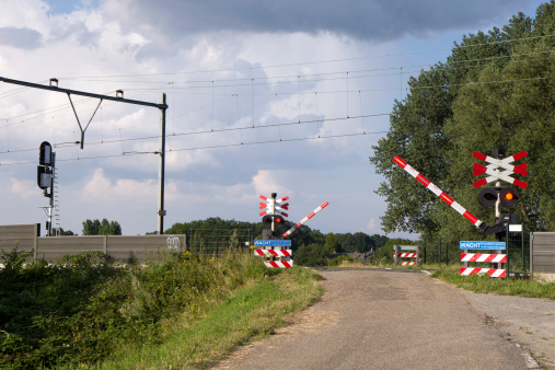 A railroad crossing closing, red lights blinking and barriers coming down. Zaltbommel, The Netherlands.