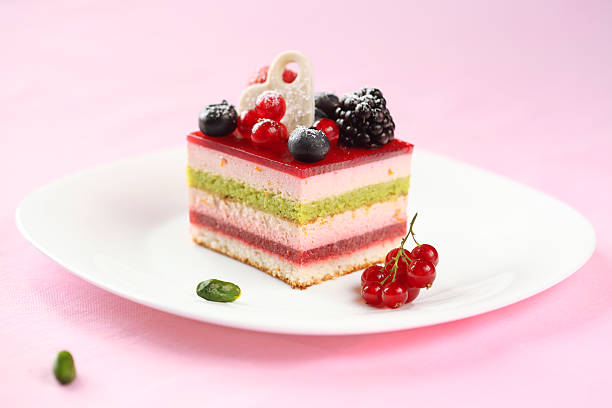 Piece of Multi-layered Berry and Pistachio Mousse Cake, on a white plate and on light pink background.