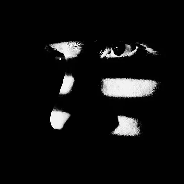 Close up of a male face illuminated through a window blind. Focus on the eye, High contrast, black & white.