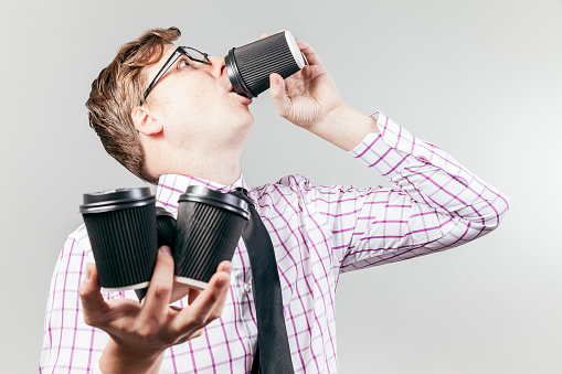 A business nerd drinks coffee out of a take away coffee cup, with 3 more in the other hand.