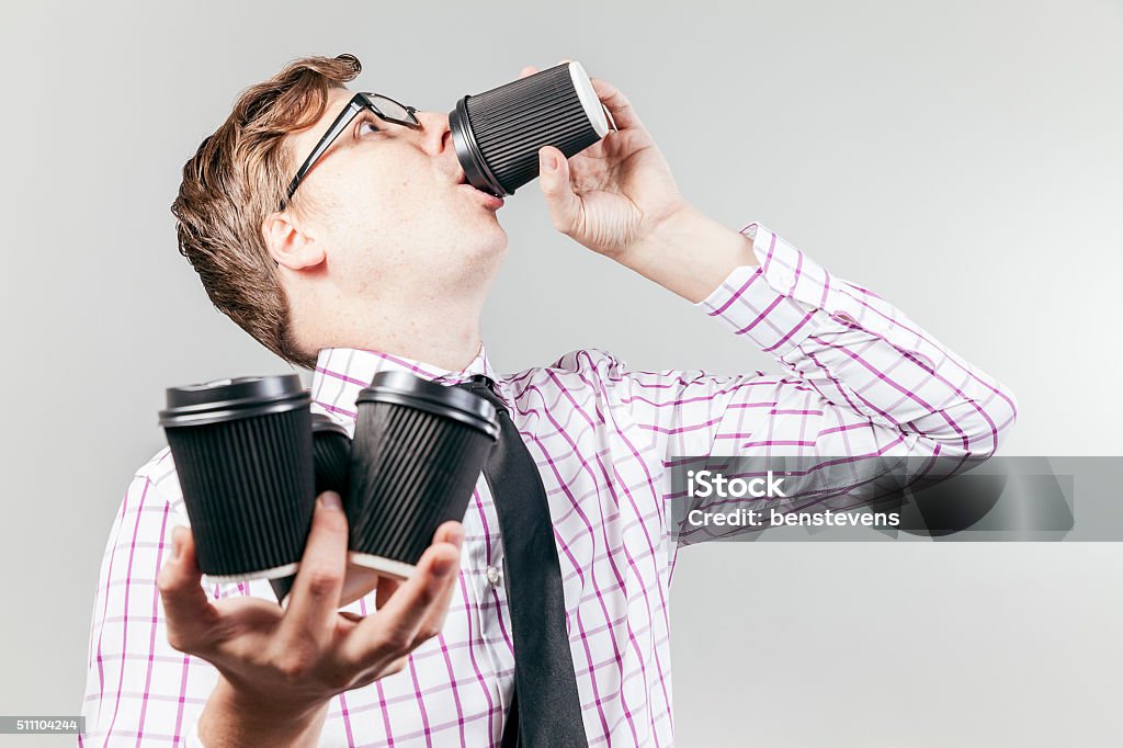 Thristy business nerd drinking coffee A business nerd drinks coffee out of a take away coffee cup, with 3 more in the other hand. Caffeine Stock Photo