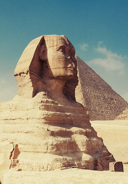 Pyramids of Giza, Giza Necropolis, Egypt - July 14, 2023: Man walking with camels at Great Sphinx of Giza. The Great Sphinx of Giza is a limestone statue of a reclining sphinx, a mythical creature with the head of a human and the body of a lion.