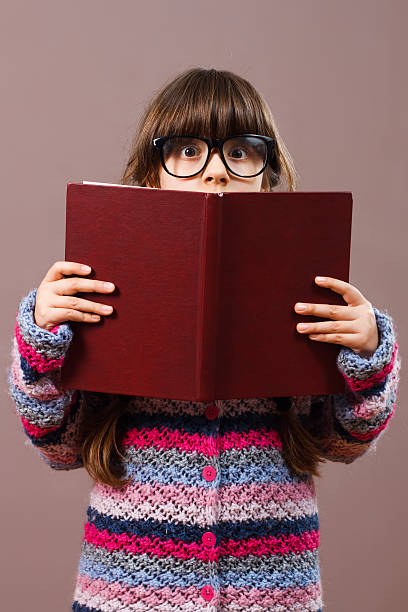istock Little girl hiding behind book 511112554