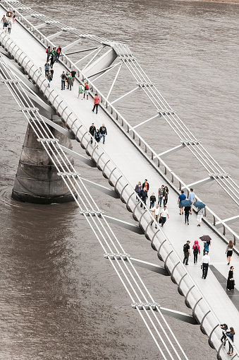 Overhead, aerial image of people and tourists walking across the Millennium Bridge in central London, UK. Vertical colour image with room for copy space.
