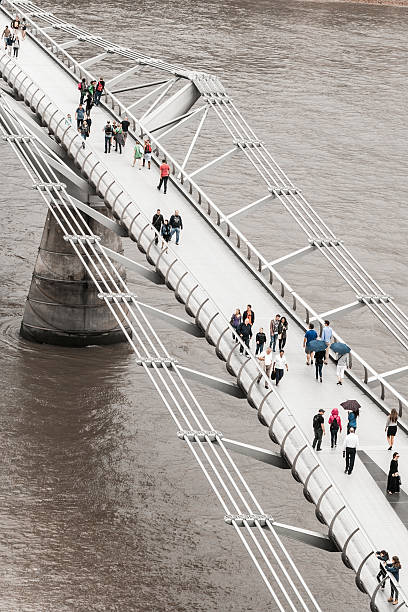 Tourists and Pedestrians walking across Millennium Bridge, London, UK Overhead, aerial image of people and tourists walking across the Millennium Bridge in central London, UK. Vertical colour image with room for copy space. thames river photos stock pictures, royalty-free photos & images