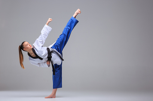 The karate girl in white kimono and black belt training karate over gray background.