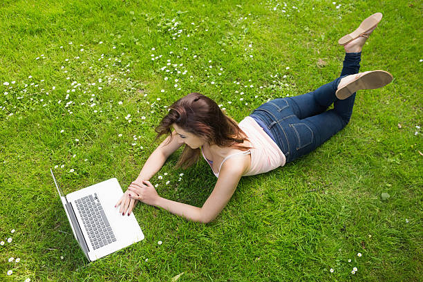 istock Pretty young woman lying on a lawn using her laptop 511132427