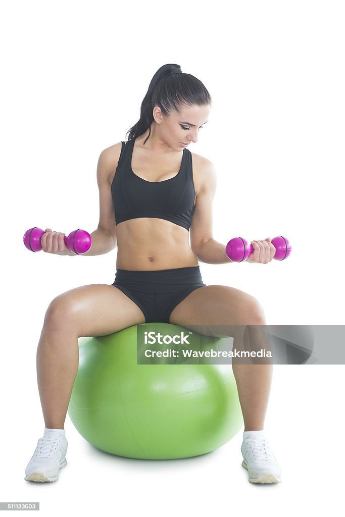 Active woman sitting on an exercise ball Sporty slim woman training her arms with dumbbells sitting on an exercise ball on white screen 20-24 Years Stock Photo