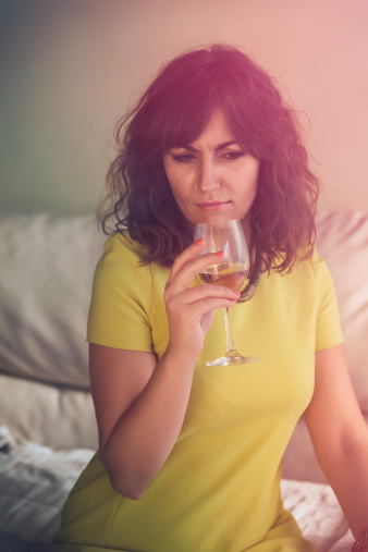 High angle view of a pensive thoughtful young woman enjoying a glass of white wine seated on a sofa with a colorful glow effect around her head, the morning after concept