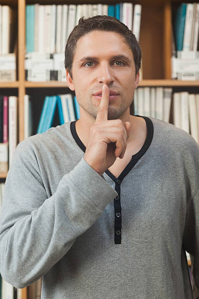 istock Male librarian making a sign to be quiet in library 511135567