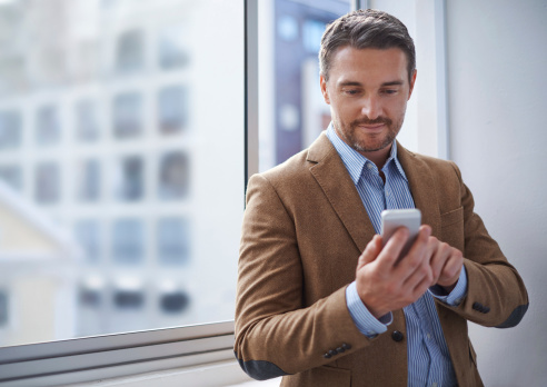 Shot of a handsome man using a cellphone by a window