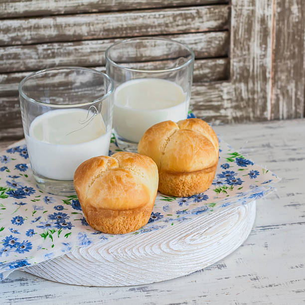 Buns and glasses of milk on a light rustic wood background.