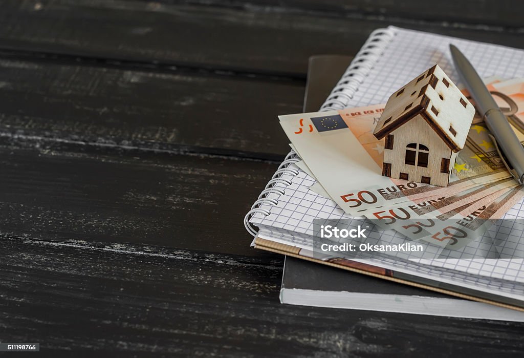 Model house, Euro banknotes, notepad on dark wooden background Model house, Euro banknotes, notepad on dark wooden background. The concept of buying, selling, trading, housing construction. Buying Stock Photo