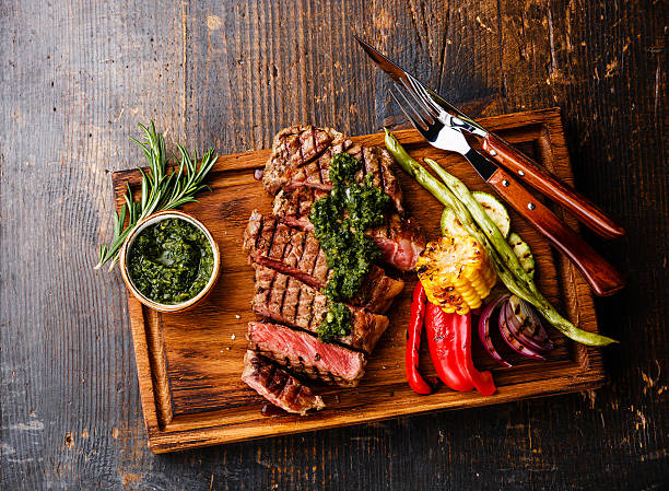 Steak with chimichurri sauce and Grilled vegetables Sliced Striploin steak with chimichurri sauce and Grilled vegetables on cutting board on dark background chimichurri stock pictures, royalty-free photos & images
