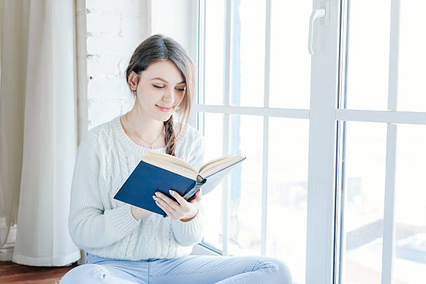 istock Young woman at home reading book 511209290