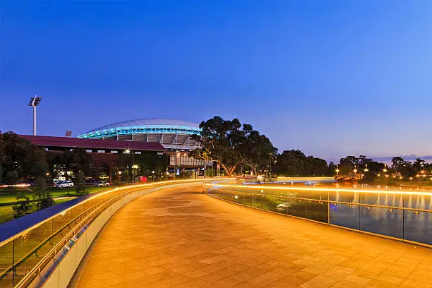 width of modern footbridge over Torrens river in Adelaide, South Australia. Bright illumination lights reflecting in calm waters at sunrise