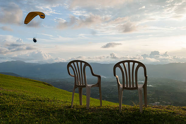A paraglider sails past two empty chairs on a hillside near sunset in Bucaramanga, Colombia.