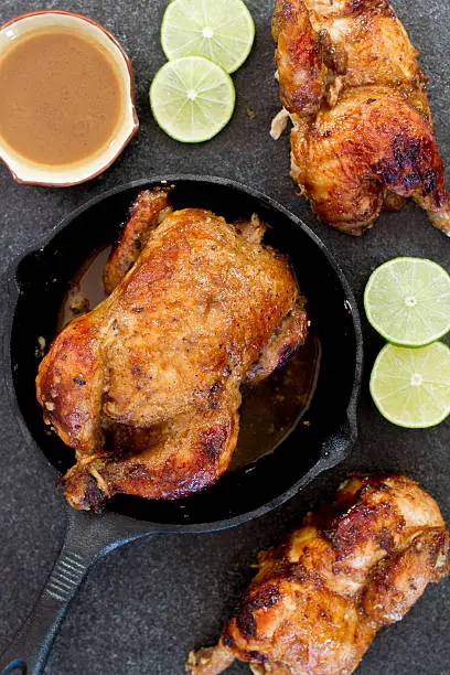 a photograph of Cornish hens, one halved and one whole, that has been basted with a lime and maple syrup glaze and roasted to perfection in a cast iron skillet.  served with a side of gravy.