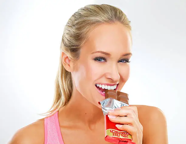 Shot of fit young woman in exercise clothes eating a chocolate bar