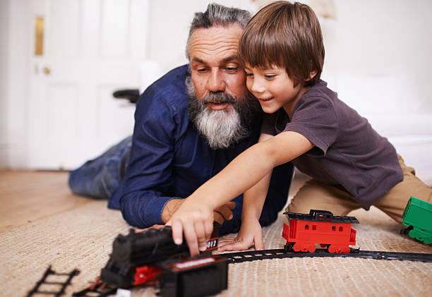 Showing grandpa my new train set Cropped shot of a grandfather watching his grandson play with a toy train miniature train stock pictures, royalty-free photos & images