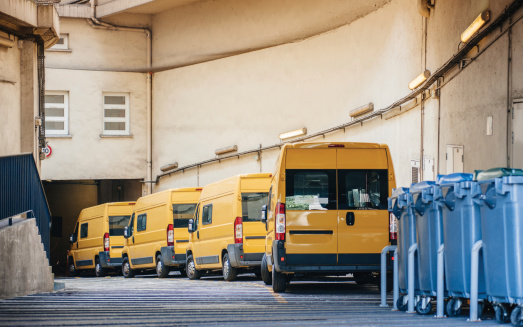 Row of yellow delivery and service van, trucks and cars in front of the entrance of a warehouse distribution logistic plant