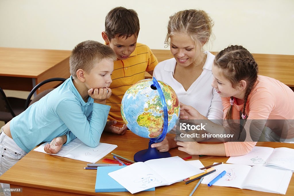 Geography lesson Portrait of cute schoolchildren and teacher looking at globe in classroom Adult Stock Photo