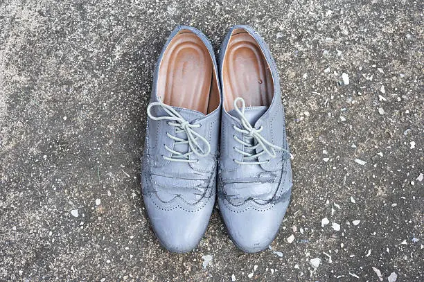 Damaged old grey brogue shoes which made from leatherette on cement back ground 
