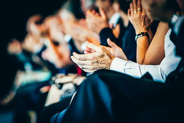 Group of businesspeople sitting in a row and applauding at seminar. Selective focus.